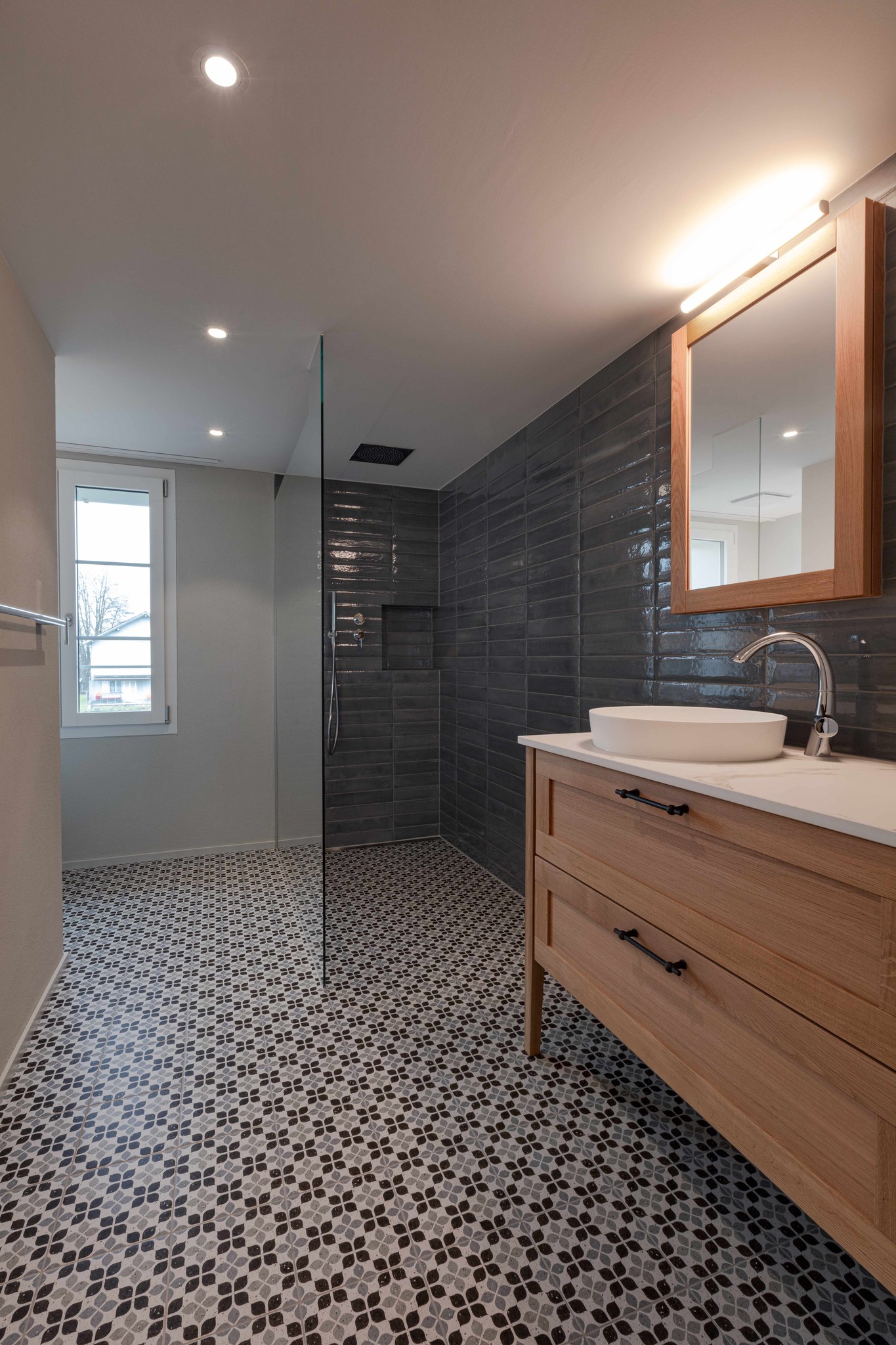 Badezimmer mit dunkler Dusche und Holzmöbel auf gemustertem Boden